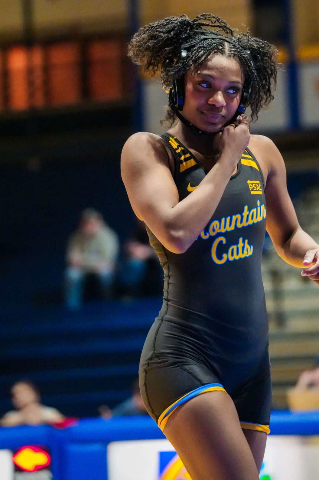 Tamara Humphries adjusting her headgear strap in a black and gold Mountain Cats singlet, looking off to the side.